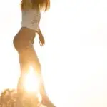 A young woman balancing on a fence during a serene sunrise, exuding freedom and joy.