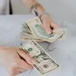 Close-up of hands counting US dollar bills on a marble table, symbolizing personal finance.